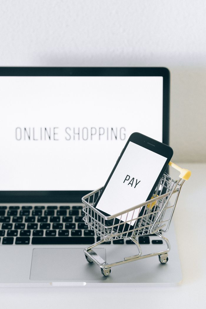 services-01 A smartphone in a miniature cart on a laptop symbolizes online shopping and digital payment.